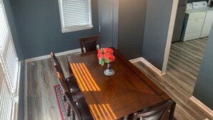 A dining area with a wooden table, chairs, a vase with flowers, a window, and a kitchen in the background. - Sweet Dreams in Sacramento (Sacramento)
