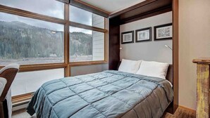 Ein Schlafzimmer mit großem Fenster, einem Bett, einem Sessel und einem kleinen Tisch.