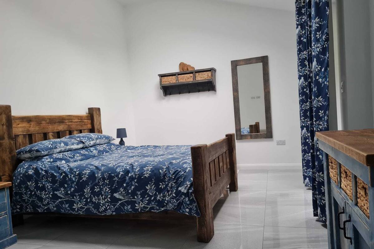 A bedroom with a wooden bed, a nightstand, a mirror, and a dresser.