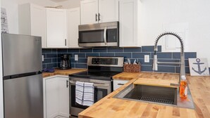 A compact kitchen with white cabinets, a stainless steel refrigerator, a microwave, a stove, and a sink with a modern faucet. - Lakeside Bungalows Unit 1&2 (Bayview)