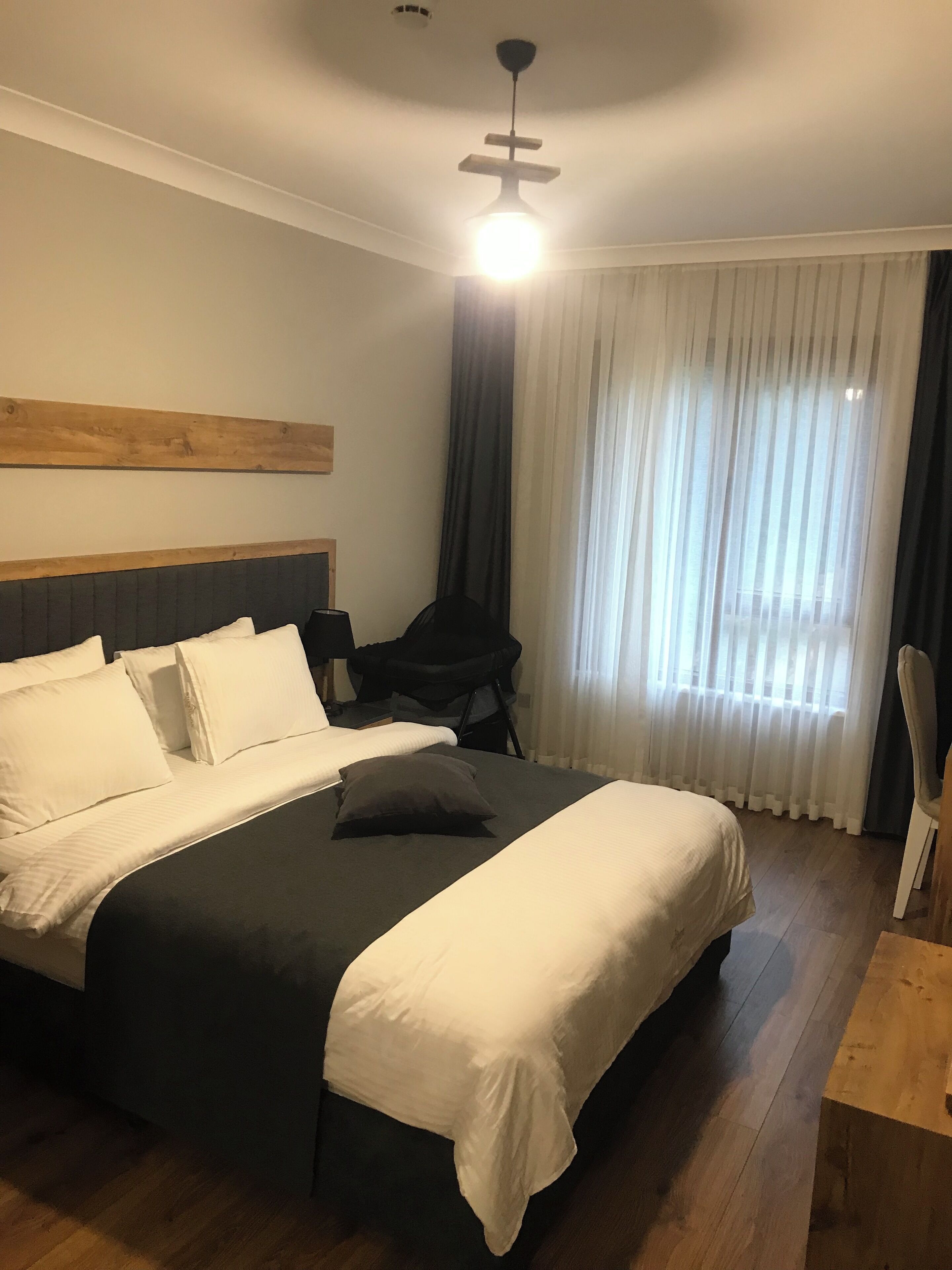 A neatly made bed with white and grey bedding, a wooden headboard, a small bedside table, and a chair.