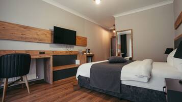 Una habitación de hotel moderna con un escritorio de madera, un televisor de pantalla plana, una cama con edredón gris y un espejo.