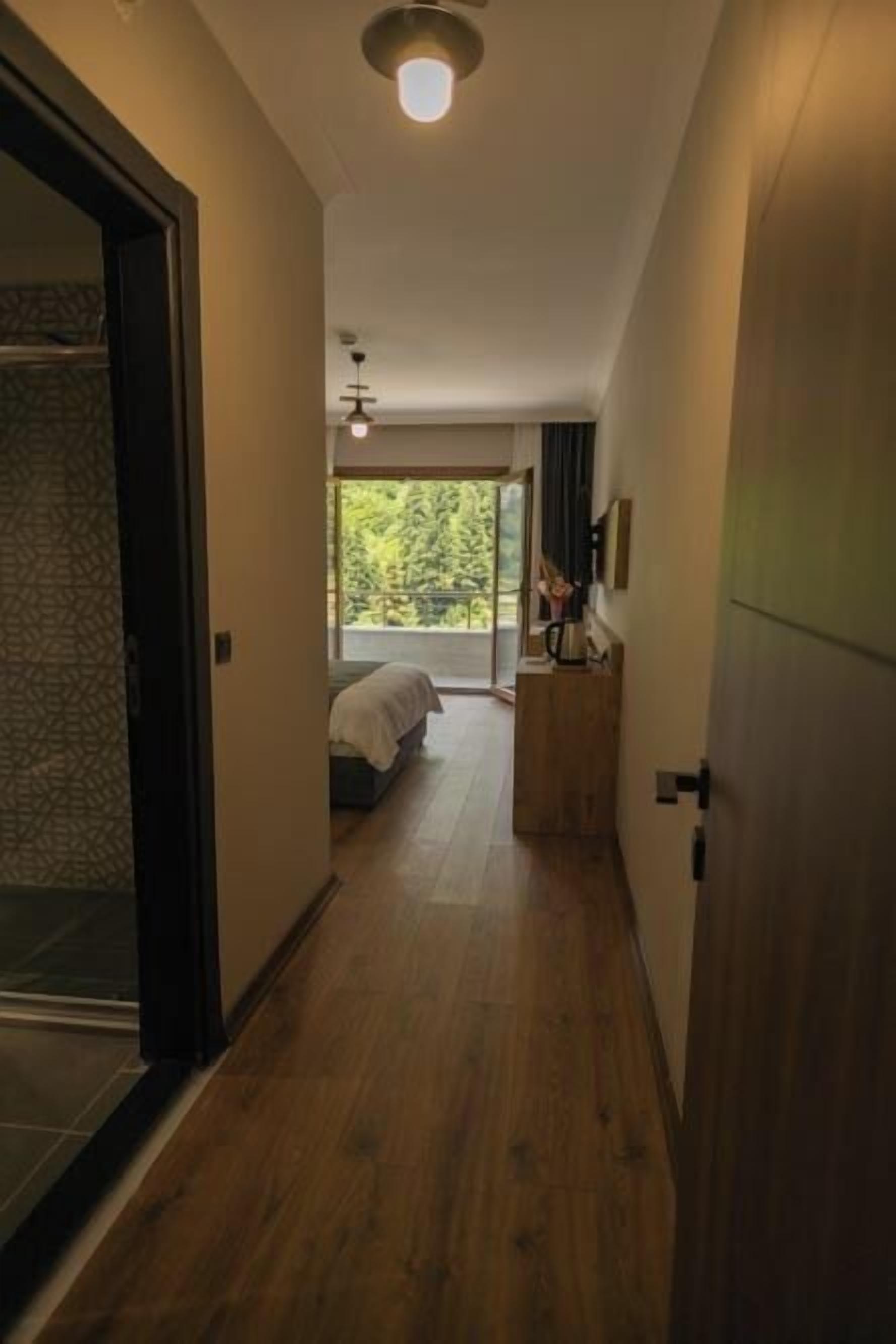 A hallway with wooden flooring leading to a bedroom with a bed and a window.