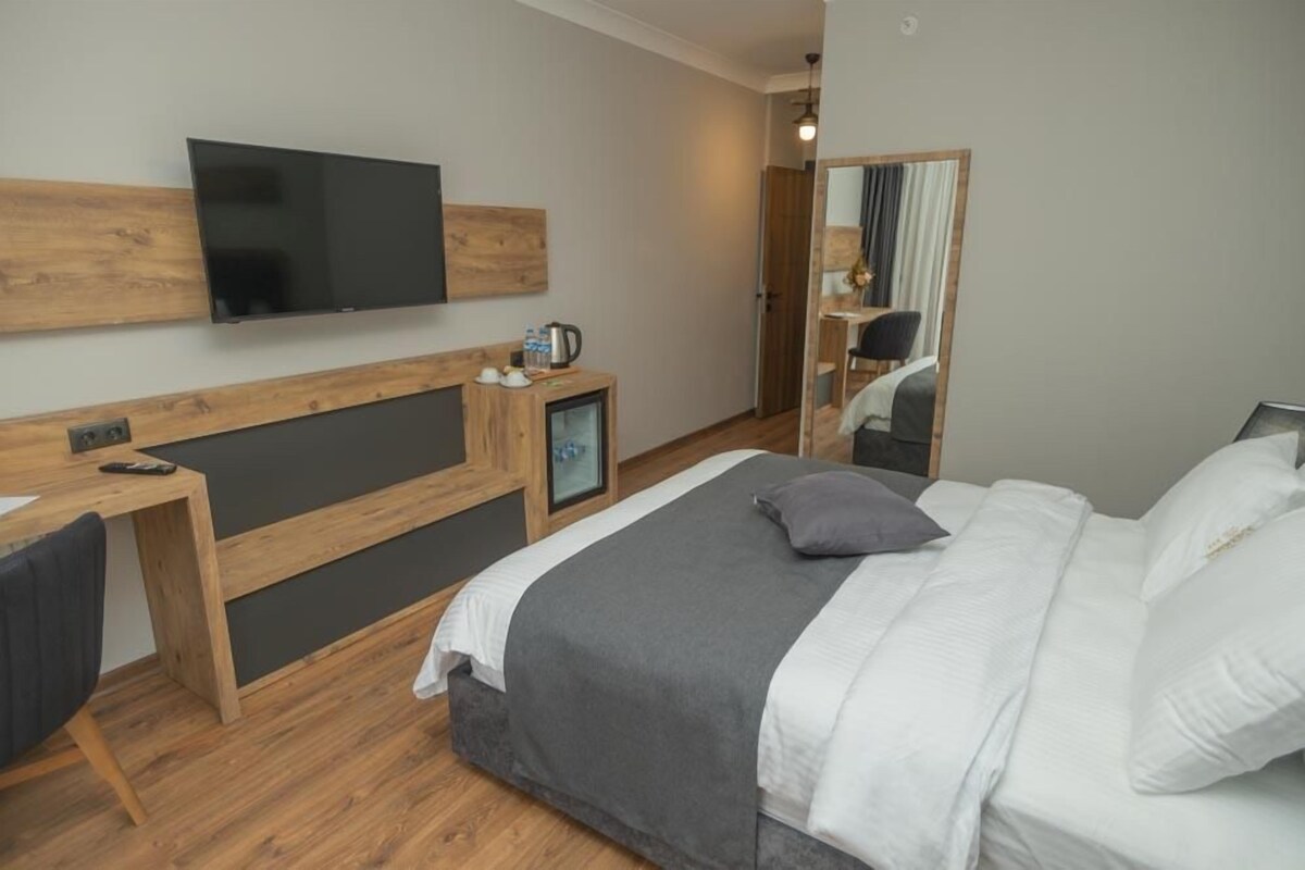 A modern hotel room with a bed, a desk, a television, and a mirror.