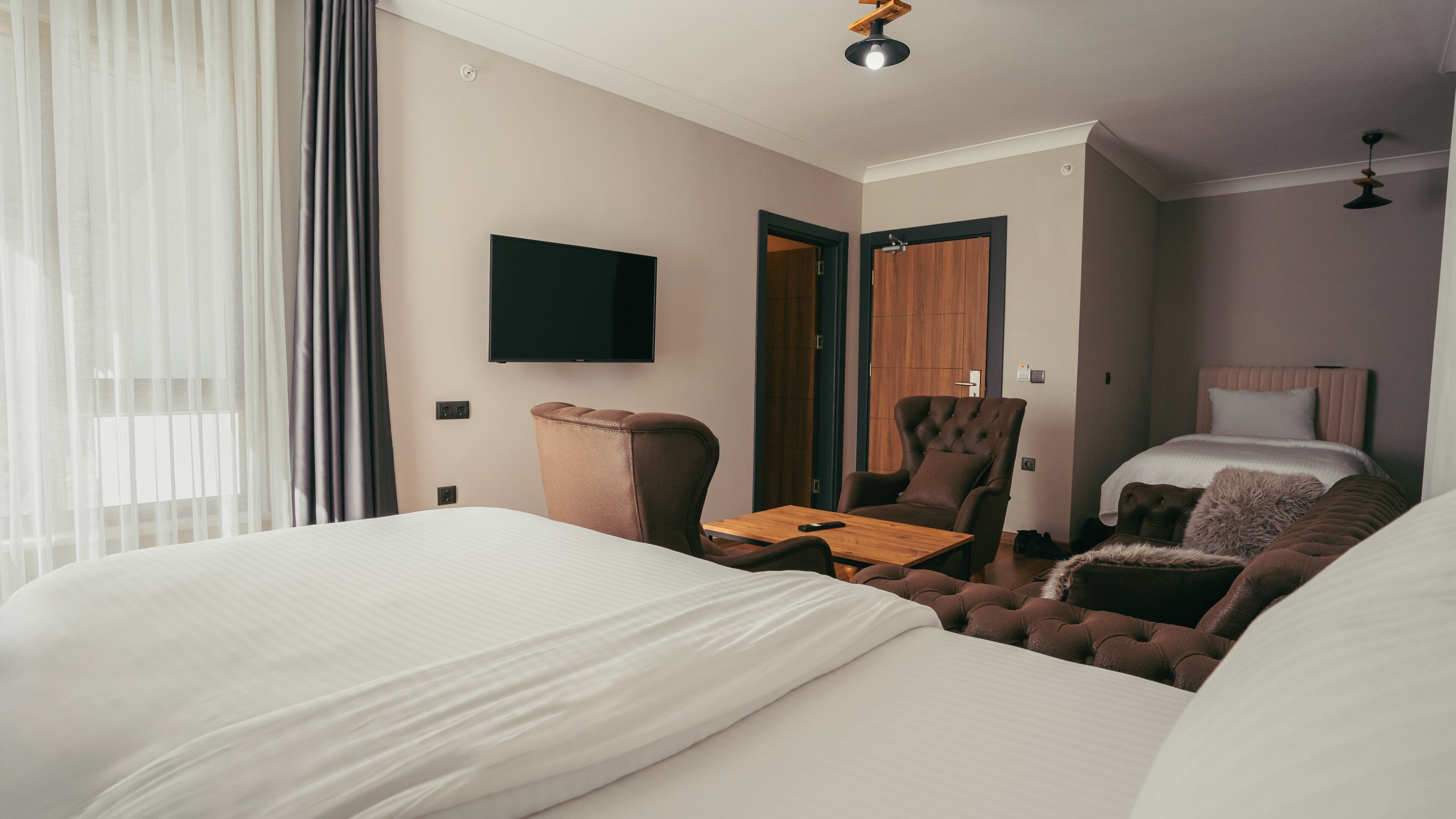 Quarto de hotel com duas camas, televisão, cadeira, mesa e porta que dá para outro cômodo.