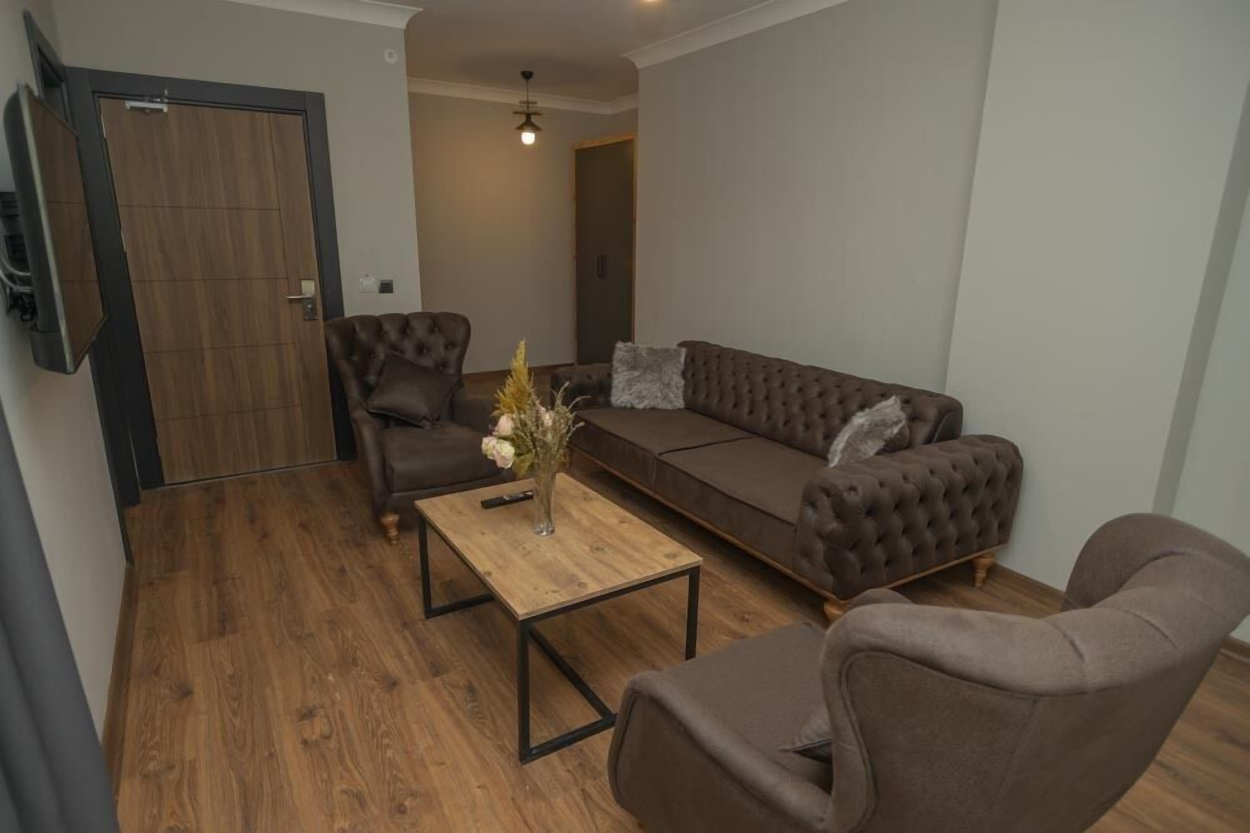 Una sala de estar con un sofá, dos sillones, una mesa de centro y un televisor montado en la pared.