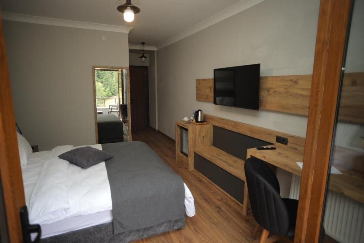 A bedroom with a bed, a desk, a chair, a television, and a window.
