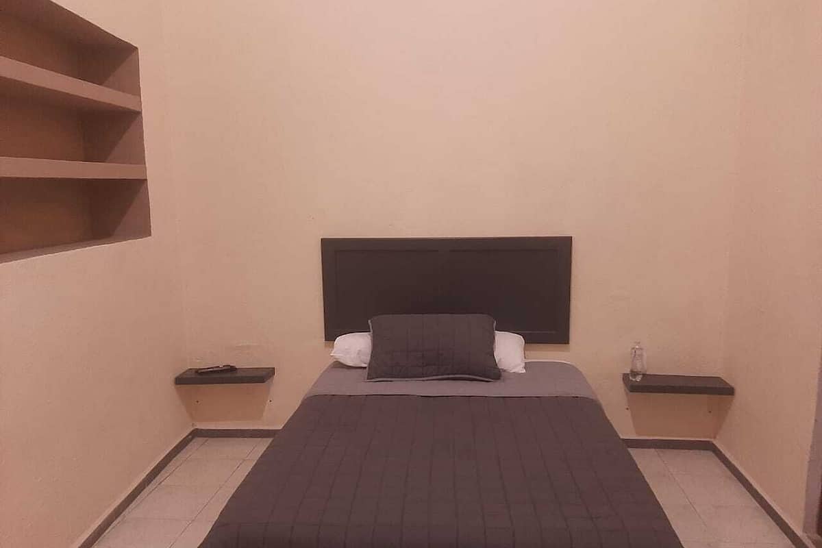A small, single-bed room with a dark headboard, two bedside tables, and a plain wall.