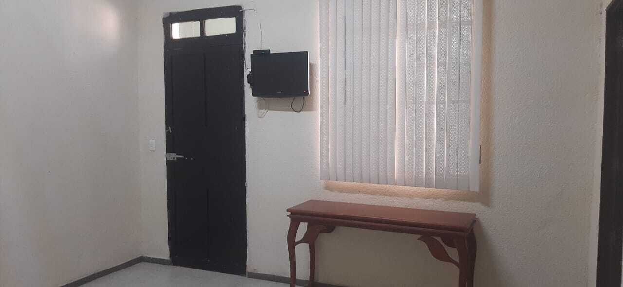 A room with a closed black door, a small wooden table, and a window with blinds.
