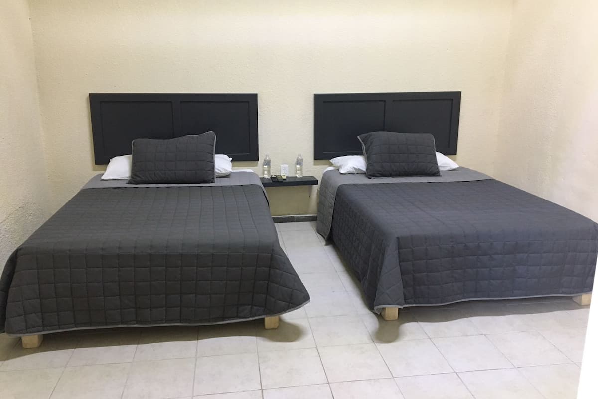 Two single beds with dark bedding, a nightstand with a lamp, and a wall-mounted phone between them.