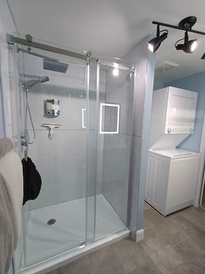 Une salle de bain moderne avec une douche à parois de verre, un porte-serviettes et un lave-linge encastré.