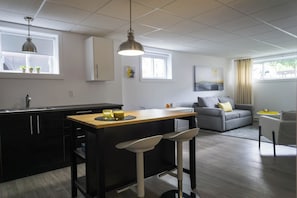 A modern kitchen with a bar area, a grey sofa, and a dining table.