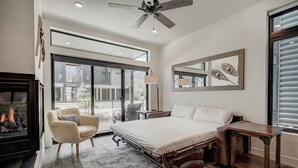 A modern bedroom with a large bed, a ceiling fan, a fireplace, and a view of the outside. - River West · Upscale Value, Centrally Located & Comfortable (Silverthorne)