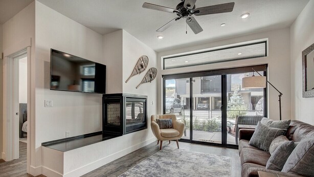 A spacious living room with a large TV, a fireplace, a ceiling fan, and a sliding glass door to the outdoors. - River West · Upscale Value, Centrally Located & Comfortable (Silverthorne)