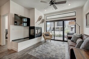 Ein geräumiges Wohnzimmer mit großem Fernseher, Kamin, Deckenventilator und einer großen Schiebeglastür zum Garten.