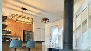 Een moderne keuken met een houtkachel, twee barkrukken en een hanglamp boven het aanrecht.