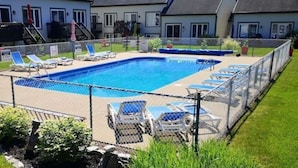 Une piscine rectangulaire entourée d’une clôture en treillis métallique, avec des chaises longues et une pelouse tout autour.