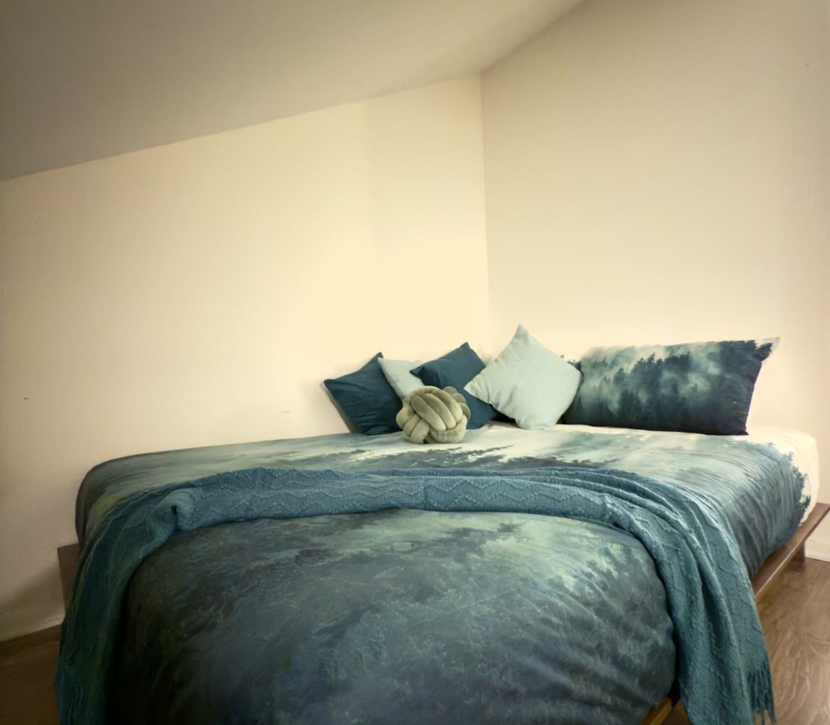 A bed with a blue and green patterned bedspread, a wooden headboard, and several pillows.