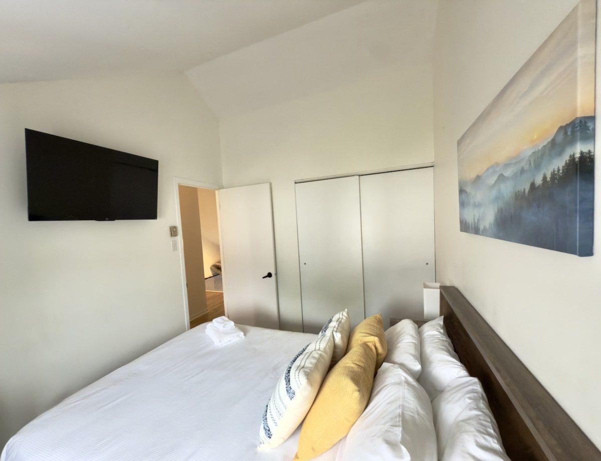 Una camera d'hotel con un letto, una TV a schermo piatto fissata al muro e un quadro sopra il letto.