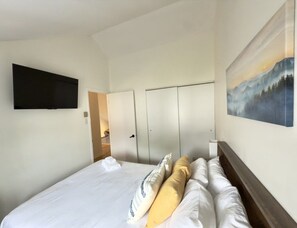 A hotel room with a bed, a flat-screen TV mounted on the wall, and a painting above the bed. - The Mont-Saint-Anne Landmark (Beaupré)