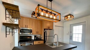 Une cuisine moderne avec des meubles en bois, des appareils en acier inoxydable, un plan de travail noir et un luminaire suspendu.