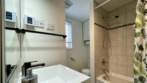 Een badkamer met een witte wastafel, een spiegel, een douche met glazen deur en een toilet.