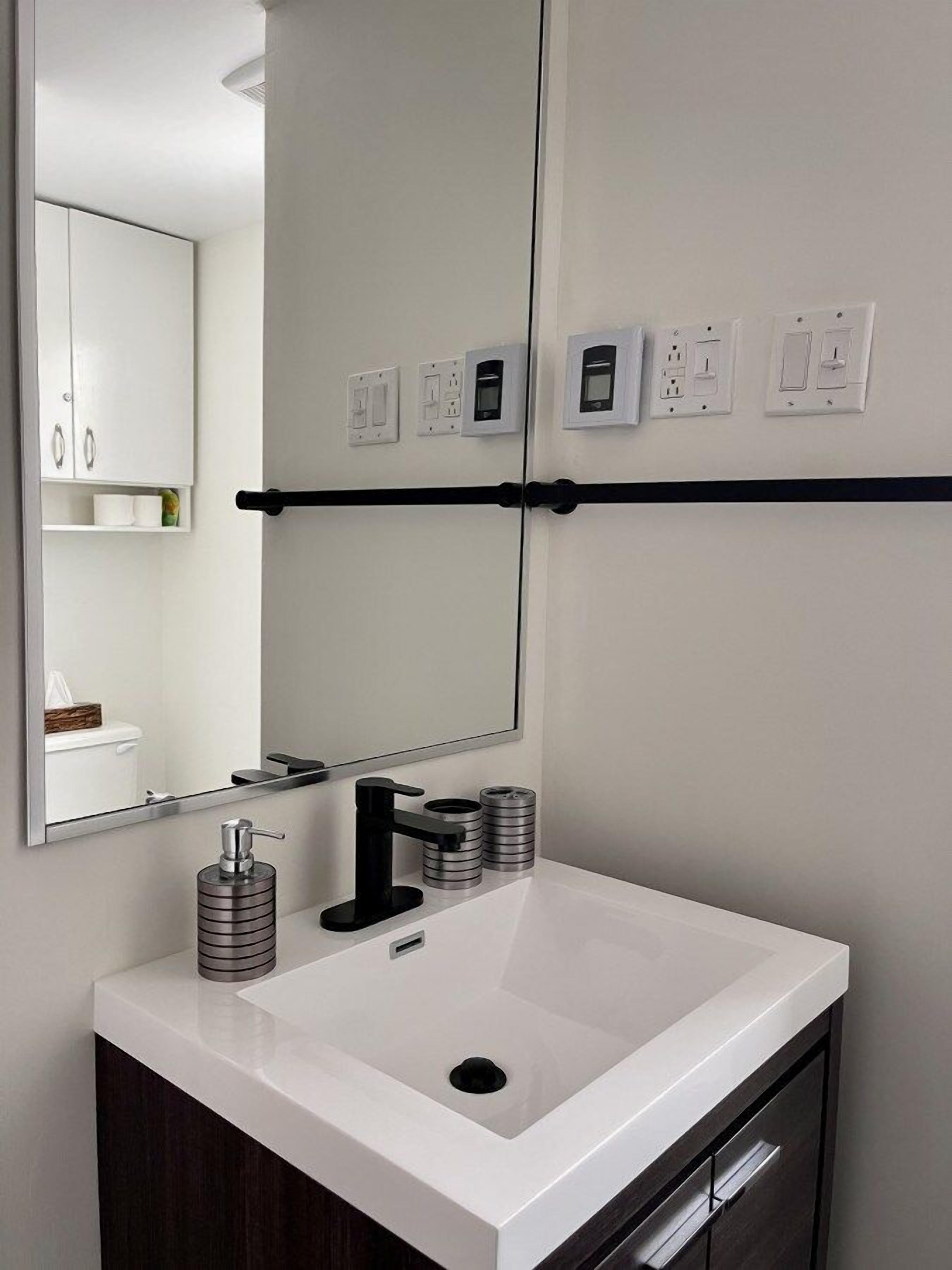 Un baño moderno con un lavamanos blanco, un espejo grande y un toallero negro.