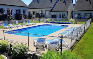 Piscina con sillas de descanso y zona vallada, rodeada de casas.