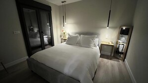 Une chambre moderne avec un grand lit, des tables de chevet, un miroir et une porte coulissante donnant sur une autre pièce.