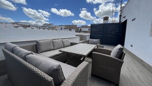 Une terrasse sur le toit, aménagée avec des meubles en osier, une table et offrant une vue sur le paysage urbain.