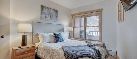 A bedroom with a bed, bedside tables, a window, and a painting on the wall.