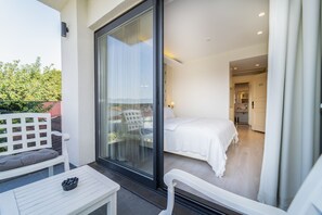 A balcony with a white table and bench, a sliding glass door leading to a bedroom with a bed and a bathroom visible. - Rooms365 (Fethiye)