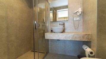 A modern bathroom with a glass-enclosed shower, a marble sink, and a hairdryer mounted on the wall.