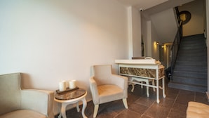 A cozy room with a sofa, armchair, small table with candles, and a marble side table. A staircase with a circular wall design is visible in the background. - Rooms365 (Fethiye)