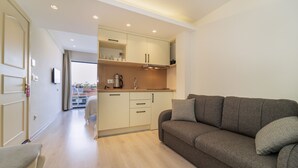A modern living room with a sofa and a dining area with a kitchen in the background. - Rooms365 (Fethiye)