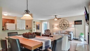 A modern living space with a dining area, a sofa, a large wall clock, and a ceiling fan. - Traverse city condo/golfing/beaches/wineries/hiking (Williamsburg)