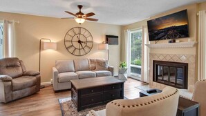 A living room with a sofa, armchair, coffee table, fireplace, TV, and a large wall clock. - Traverse city condo/golfing/beaches/wineries/hiking (Williamsburg)