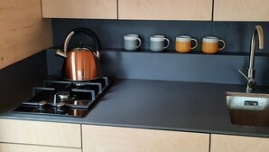 A compact kitchen with wooden cabinets, a gas stove, a kettle, and a set of mugs. - Loch Awe Luxury Eco Cabins (Dalmally)