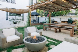 An outdoor patio with wicker furniture, a fire pit, and a pergola with string lights.