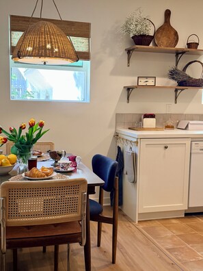 A dining area with a table set for breakfast, a wicker chair, and a hanging light fixture.