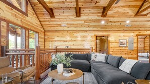 A cozy cabin interior with a wooden ceiling, a sofa, a coffee table, and a balcony with a railing. - Hot Tub + Pool Table + Pavilion | Smoky Mountain Views | Ridge View (Sevierville)