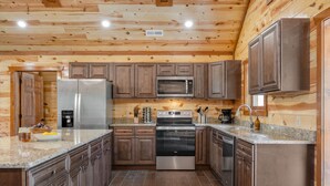 A modern kitchen with wooden walls, stainless steel appliances, granite countertops, and a central island. - Hot Tub + Pool Table + Pavilion | Smoky Mountain Views | Ridge View (Sevierville)