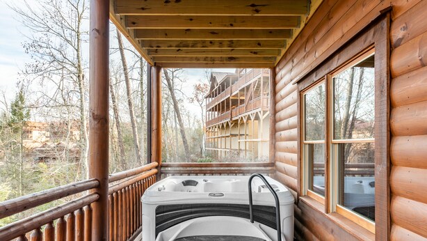 A wooden cabin with a hot tub on a porch, overlooking a forested area. - Hot Tub + Pool Table + Pavilion | Smoky Mountain Views | Ridge View (Sevierville)