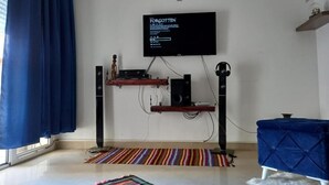 En stue med et fladskærms-TV på væggen, et lydsystem og en blå sofa.