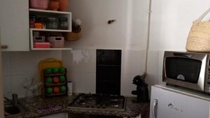 Et kompakt køkken med hvide skabe, en gasblus, en mikrobølgeovn og et lille køleskab.