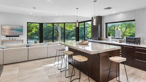 Una cocina moderna con una isla grande, taburetes de bar y vistas a zonas verdes.