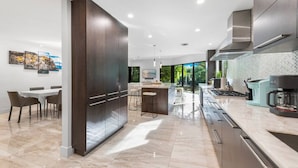 Una cocina moderna con armarios oscuros, una isla central y un comedor con mesa y sillas.