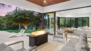 Una sala de estar moderna con chimenea, ventanas amplias y vistas a un jardín.