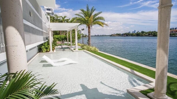 A modern outdoor pool area with a clear view of the water, palm trees, and a distant city skyline. - Luxury Vacation Rental Waterfront Condo Bal Harbour Miami Beach (Bay Harbor Islands)