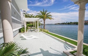 A modern outdoor pool area with a clear view of the water, palm trees, and a distant city skyline.